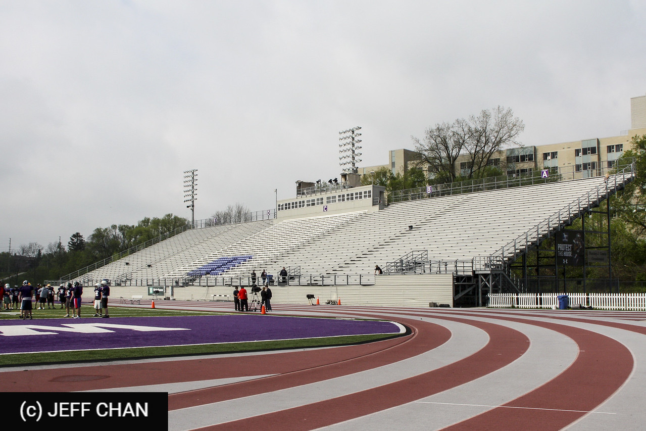 Wide view of an empty stadium grandstand with a running track and field under a cloudy sky, calm and open in feeling